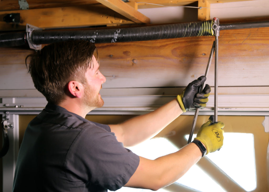 Technician repairing a garage door spring with a tool